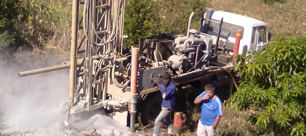 Drill crew operating the rig as rock dust blows from the hole