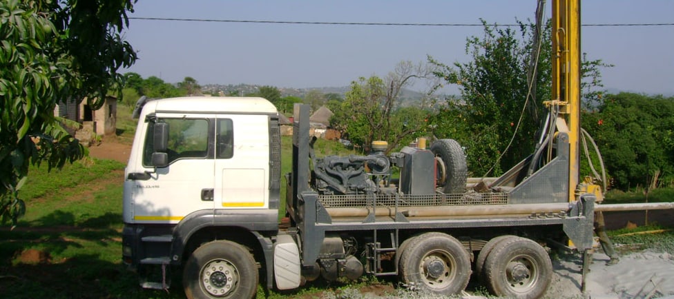 Drilling truck with mast raised on a green hillside property